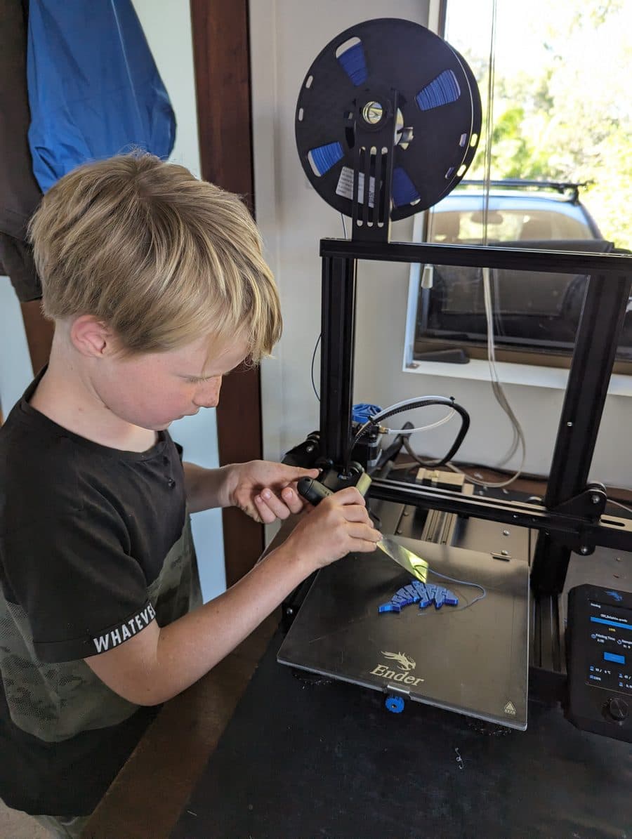 A child working a just-finished print off the bed of a 3D printer