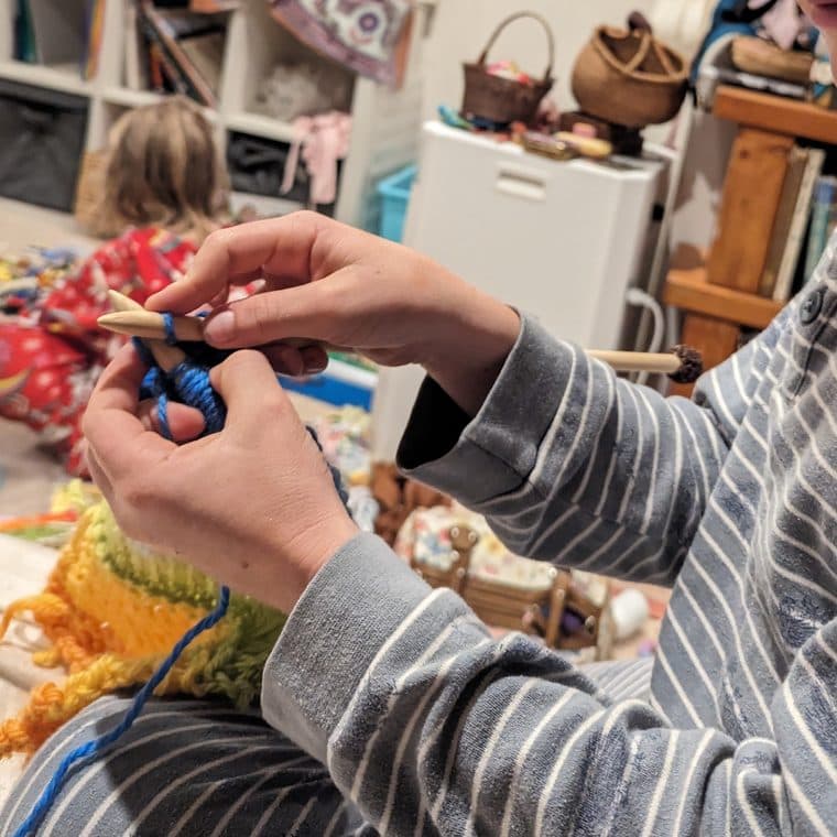 A child knitting a row on wooden needles